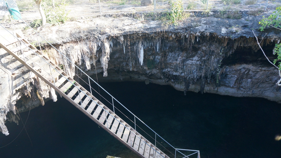 Stalactites on roof of cenote, stairs to water in foreground